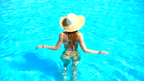 young-girl-in-sexy-bathing-suit-and-hat-walks-into-the-water-in-the-pool