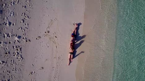 v03998-Aerial-flying-drone-view-of-Maldives-white-sandy-beach-2-people-young-couple-man-woman-romantic-love-on-sunny-tropical-paradise-island-with-aqua-blue-sky-sea-water-ocean-4k