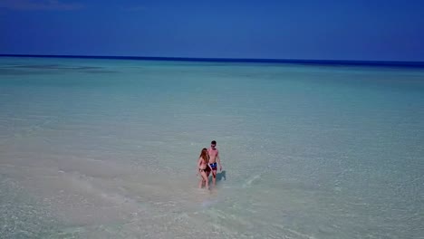 v03876-Aerial-flying-drone-view-of-Maldives-white-sandy-beach-2-people-young-couple-man-woman-romantic-love-on-sunny-tropical-paradise-island-with-aqua-blue-sky-sea-water-ocean-4k