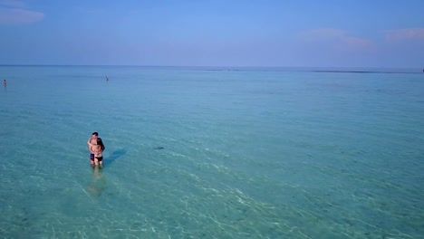 v03976-vuelo-drone-vista-aérea-de-Maldivas-playa-2-personas-pareja-hombre-mujer-amor-romántico-en-la-isla-de-paraíso-tropical-soleado-con-cielo-azul-aqua-agua-mar-4k