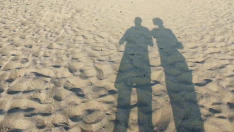 Pareja-de-jóvenes-amantes-caminando-por-la-playa-con-sombras-romántico-en-la-arena