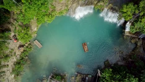 Drone-shot-aerial-view-of-young-woman-bamboo-rafting-at-tropical-waterfall.-4K-resolution-video,-shot-in-the-Philippines.-People-travel-fun-vacations-adventure-concept