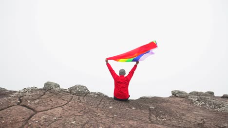 man-raise-rainbow-colour-LGBTI-flag-waving-in-hard-wind-on-mountain-top-viewpoint