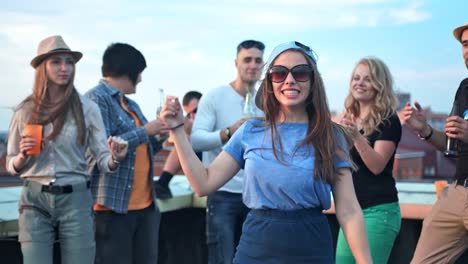 Young-woman-dancing-in-the-middle-of-crowds-with-raising-arms-at-rooftop-party