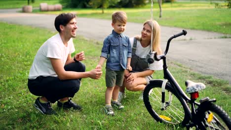 Padres-amorosos-hacen-sorpresa-hijo-cerrando-los-ojos-y-dándole-nueva-bicicleta-como-presente,-feliz-muchacho-mirando-bici-y-hablando-con-la-madre-y-padre.