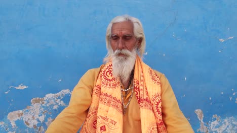 Sadhu,-Santo-hindú,-sentada-fuera-de-un-templo-de-meditación-contra-una-pared-azul