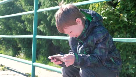 The-boy-plays-a-game-on-his-mobile-phone-while-sitting-in-the-Park.