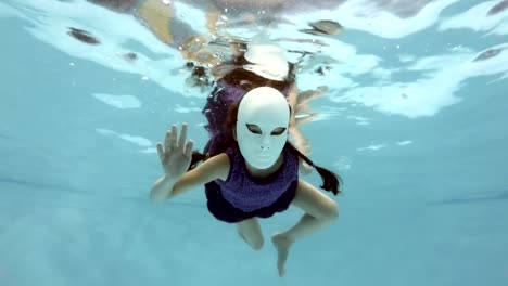 Ein-kleines-Mädchen-in-eine-fabelhafte-Weiße-Maske-schwimmt-und-unter-Wasser-stellt,-schaut-in-die-Kamera-und-seine-Hände-winken.