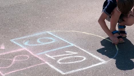 Boy-is-drawing-hopscotch-on-the-asphalt.-Painting-a-sun.