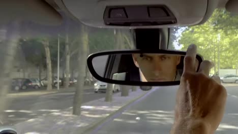 Serious-male-driver-adjusting-car-mirror-during-ride