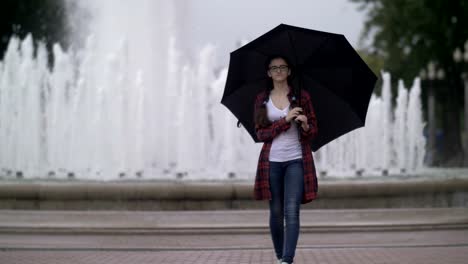 Mädchen-mit-Regenschirm-im-Park-auf-dem-Hintergrund-eines-Brunnens,-schaut-in-die-Kamera