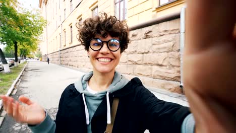 Point-of-view-shot-of-pretty-girl-looking-at-camera-and-talking-making-video-call-communicating-with-friends.-Woman-is-wearing-glasses-and-trendy-casual-clothing.