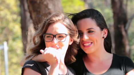 Two-girlfriends-together-walking-at-the-park-embracing-each-other-laughing