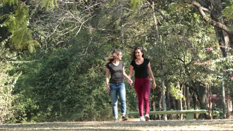 Two-girlfriends-together-walking-at-the-park-embracing-each-other-laughing