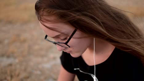 Teenage-girl-with-eyeglasses-sitting-on-the-ground-and-listening-to-the-music,-close-up