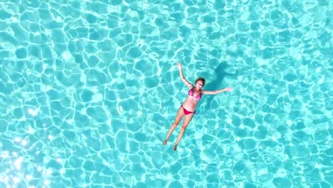 Aerial-spinning-view-of-an-attractive-woman-floating-in-crystal-clear-sea