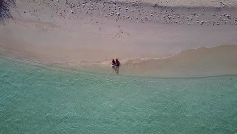 v03929-Aerial-flying-drone-view-of-Maldives-white-sandy-beach-2-people-young-couple-man-woman-romantic-love-on-sunny-tropical-paradise-island-with-aqua-blue-sky-sea-water-ocean-4k