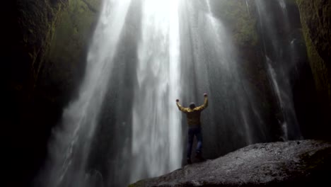 Young-traveling-man-walking-near-the-powerful-Gljufrabui-waterfall-in-Iceland.-Male-jumping-of-joy-and-happy