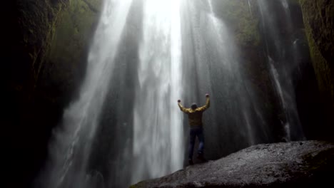 Junger-Reisender-Mann-zu-Fuß-in-der-Nähe-des-mächtigen-Gljufrabui-Wasserfalls-in-Island.-Männliche-Freude-springen-und-glücklich