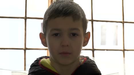 portrait-emaciated-refugee-boy-stands-alone-near-a-broken-window,-looking-into-the-camera