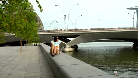 Una-mujer-se-sienta-sobre-un-parapeto-en-el-terraplén-del-río