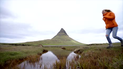 Young-woman-in-Iceland-jumping-over-fjord-river-at-famous-Kirkjufell-mountain