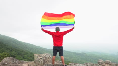 hombre-levantar-bandera-LGBTI-de-color-arco-iris-ondeando-en-duro-viento-en-el-mirador-de-alta-montaña