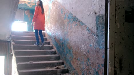 Woman-in-a-red-cloak-inspects-destroyed-building-after-the-disaster-earthquake,-flood,-fire.-Go-up-the-stairs.