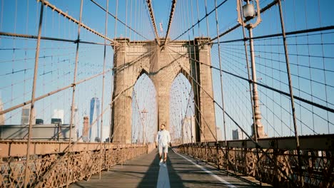 Positive-male-European-tourist-walking-towards-camera,-smiling-and-looking-around-along-Brooklyn-Bridge,-New-York-4K