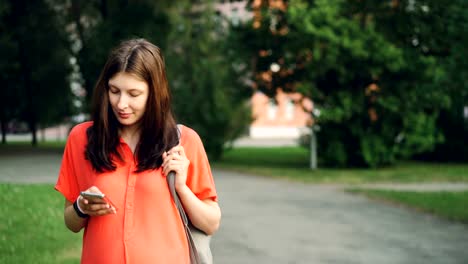 Mujer-bonita-embarazada-está-utilizando-smartphone-mirar-pantalla-caminando-en-el-parque-en-día-de-verano.-La-tecnología-moderna,-estilo-de-vida-saludable-y-el-concepto-de-embarazo.