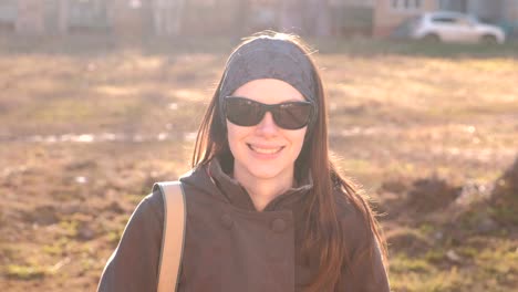 Joven-hermosa-morena-en-gafas-de-sol-mira-a-la-cámara-y-sonríe-sentado-en-el-parque.