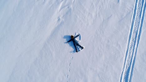 Woman-makes-snow-angel-laying-in-the-snow.-Aerial-video.-Camera-moves-away-slowly.