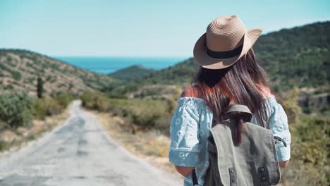 Mujer-de-caminante-de-turismo-trasera-vista-va-en-camino-rodeado-de-montañas-y-colinas