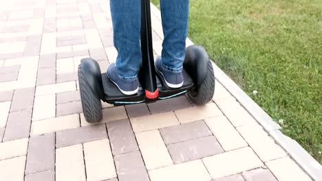 Person's-legs-in-sneakers-rolling-on-gyro-scooter-on-paving-road.