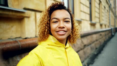 Point-of-view-shot-of-attractive-African-American-girl-vlogger-looking-at-camera,-speaking-and-waving-hand-recording-video-for-her-internet-blog-about-urban-life.