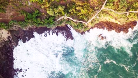 4K-top-down-aerial-drone-of-crashing-waves-on-cliff-and-long-wooden-platform-at-Timang-beach.