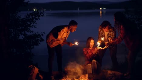 Fürsorgliche-Freunde-Touristen-sind-Mädchen-zum-Geburtstag-Kuchen-bringen-und-bengalische-Lichter-brennen-gratulieren,-Frau-bläst-Kerzen,-hält-Sparker-und-schreien.