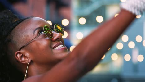 Joven-negro-a-mujer-que-lleva-gafas-de-sol-redondas-mirando-hacia-arriba,-vista-lateral,-tiro-de-cabeza,-luces-bokeh-en-fondo