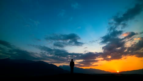 El-hombre-de-pie-sobre-una-montaña-contra-una-puesta-de-sol-con-la-luz-del-norte.-lapso-de-tiempo