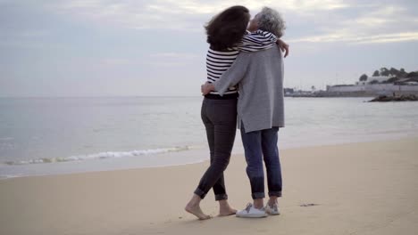 Happy-senior-mother-and-adult-daughter-hugging-on-sandy-beach.