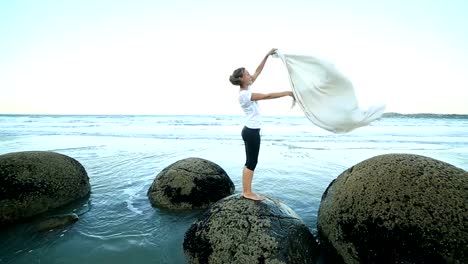 One-female-stands-on-boulder,-holds-blanket-in-the-air