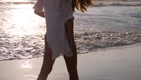 Woman-walking-on-sandy-beach-near-the-ocean.-Young-beautiful-girl-enjoying-life-and-going-at-sea-shore.-Summer-vacation-or-holiday.-Marine-landscape-at-background.-Rear-back-view