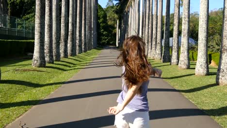 Young-beautiful-woman-jogging-and-spinning-along-exotic-parkland-and-having-fun.-Happy-girl-is-running-in-tropical-park.-Freedom-travel-concept.-Summer-vacation-trip-Rear-back-view