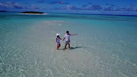 v03922-Aerial-flying-drone-view-of-Maldives-white-sandy-beach-2-people-young-couple-man-woman-romantic-love-on-sunny-tropical-paradise-island-with-aqua-blue-sky-sea-water-ocean-4k