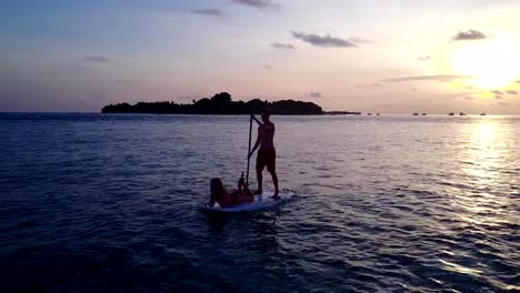 v04104-Aerial-flying-drone-view-of-Maldives-white-sandy-beach-2-people-young-couple-man-woman-paddleboard-rowing-sunset-sunrise-on-sunny-tropical-paradise-island-with-aqua-blue-sky-sea-water-ocean-4k