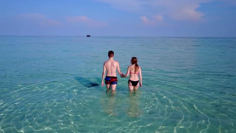 v04004-Aerial-flying-drone-view-of-Maldives-white-sandy-beach-2-people-young-couple-man-woman-romantic-love-on-sunny-tropical-paradise-island-with-aqua-blue-sky-sea-water-ocean-4k