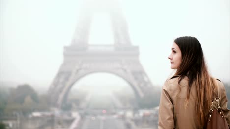 Back-view-of-young-stylish-woman-standing-in-front-of-Eiffel-tower-and-looking-on-famous-sight-if-Paris,-France