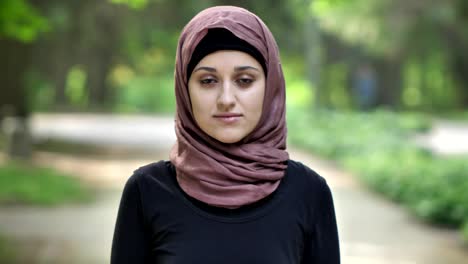 Portrait-of-a-young-sad-girl-in-hijab,-outdoor,-in-a-park-in-the-background.-50-fps