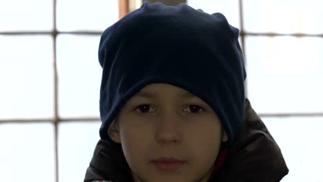 portrait-boy-stands-alone-near-a-broken-window,-looking-into-the-camera