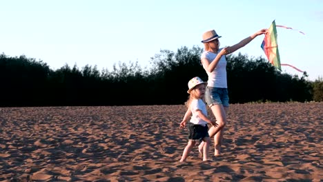 Preciosa-rubia-en-un-sombrero-de-la-mamá-y-la-hija-lanza-una-cometa-en-la-playa.